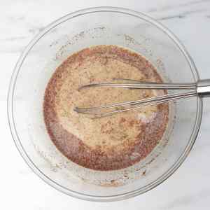 A mixing bowl containing a creamy mixture with cinnamon and a whisk.