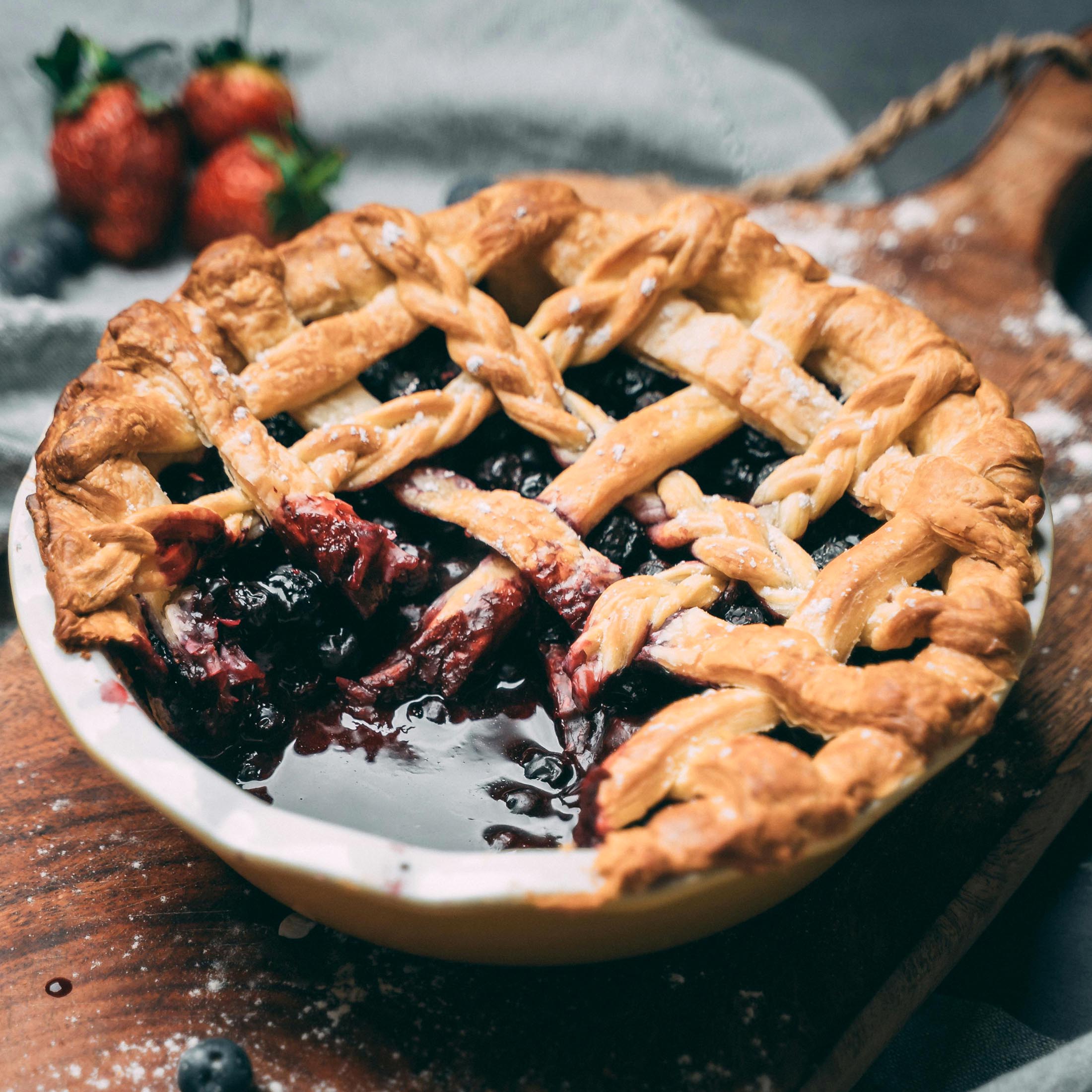A close-up of a berry pie with a golden lattice crust, placed on a wooden surface.