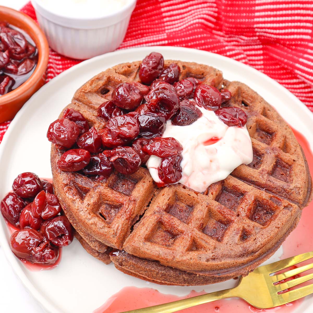Waffles de chocolate Floresta Negra Waffles de chocolate cobertos com cerejas e creme, servidos em um prato.