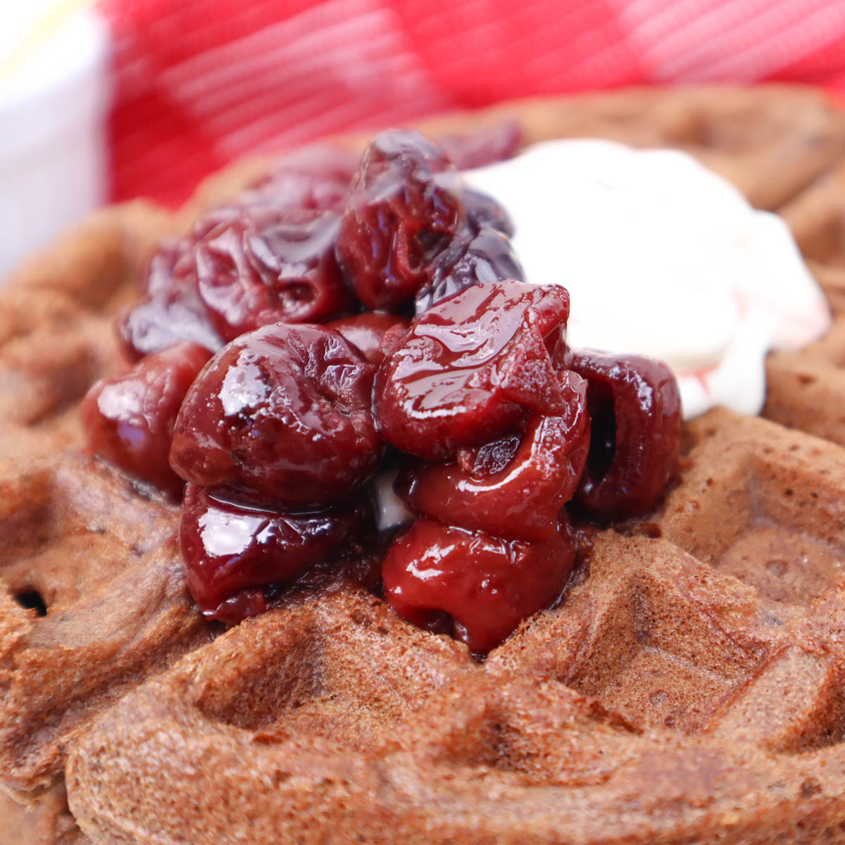 Waffles de chocolate Floresta Negra Imagem em close-up de um waffle de chocolate coberto com cerejas e chantilly.