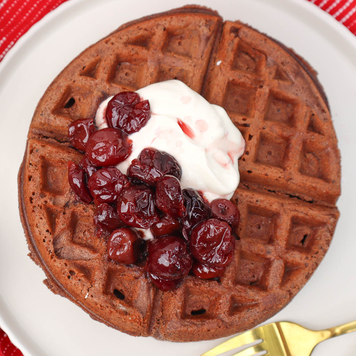 Waffles de chocolate Floresta Negra Um prato de waffles de chocolate coberto com cerejas e chantilly.