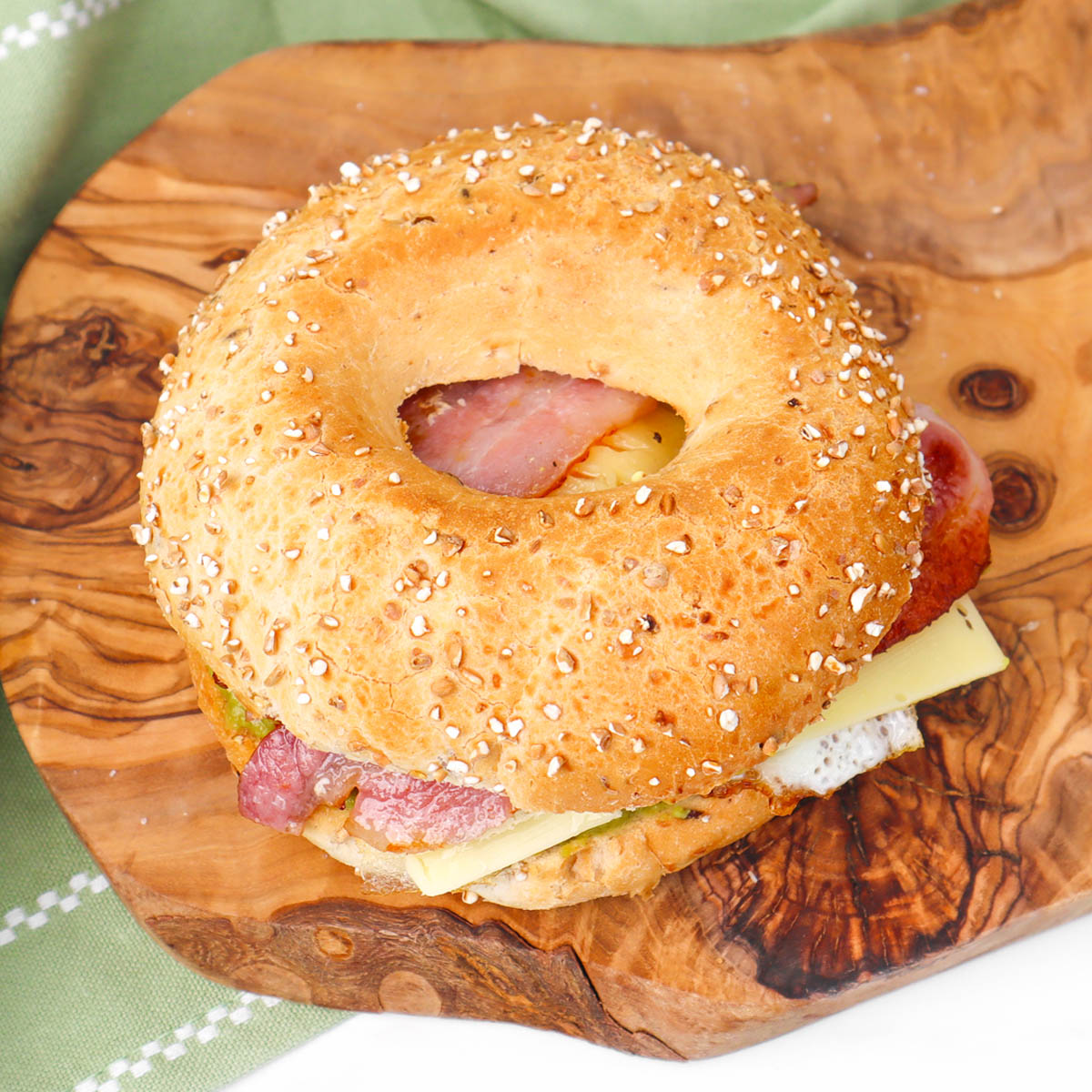 Bagel du petit-déjeuner Un bagel grillé garni de bacon, de fromage et de guacamole, servi sur une planche en bois.