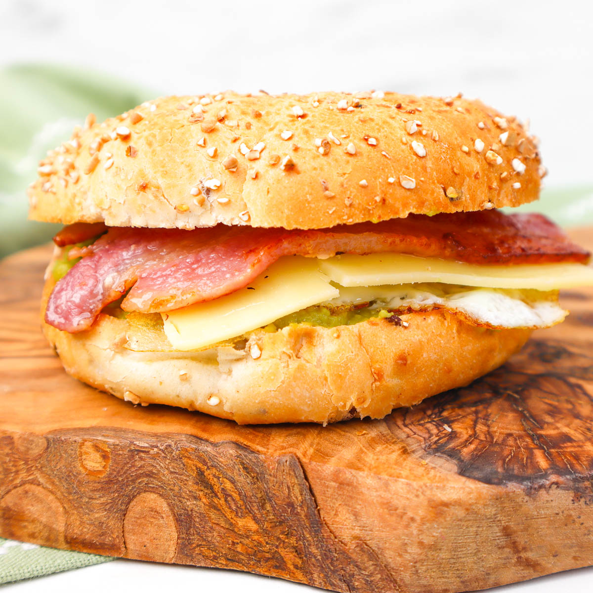 A toasted bagel filled with bacon, cheese, and egg on a wooden cutting board.