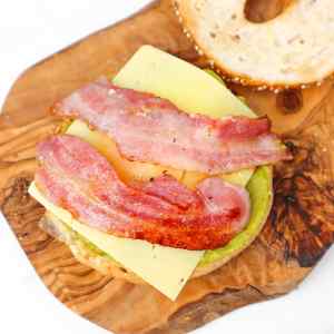Un bagel garni de bacon, de fromage et d'avocat, servi sur une planche en bois.
