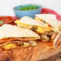 Stack of breakfast quesadillas with eggs and jalapeños on a wooden board.