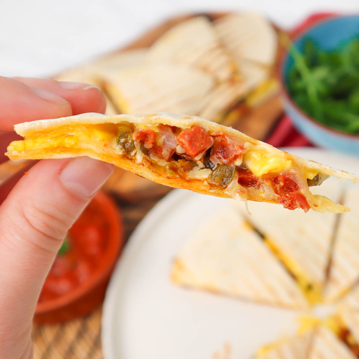 Quesadillas du petit-déjeuner Une main tenant une quesadilla de petit-déjeuner coupée en tranches et garnie d'œufs, de fromage et de légumes.
