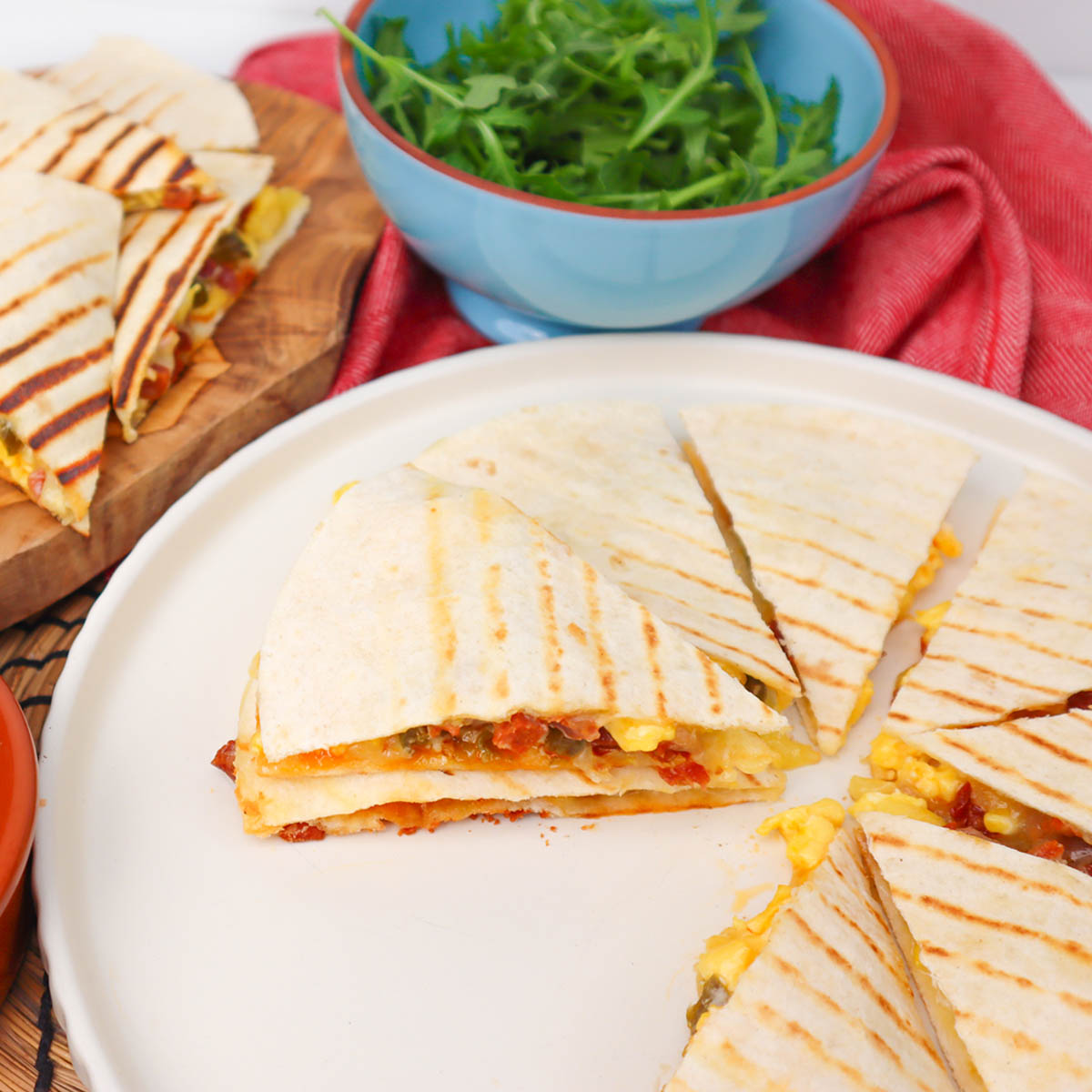 Quesadillas du petit-déjeuner Quesadillas coupées en tranches pour le petit-déjeuner, avec œufs et garnitures, servies sur une assiette, accompagnées d'un bol de légumes verts frais.