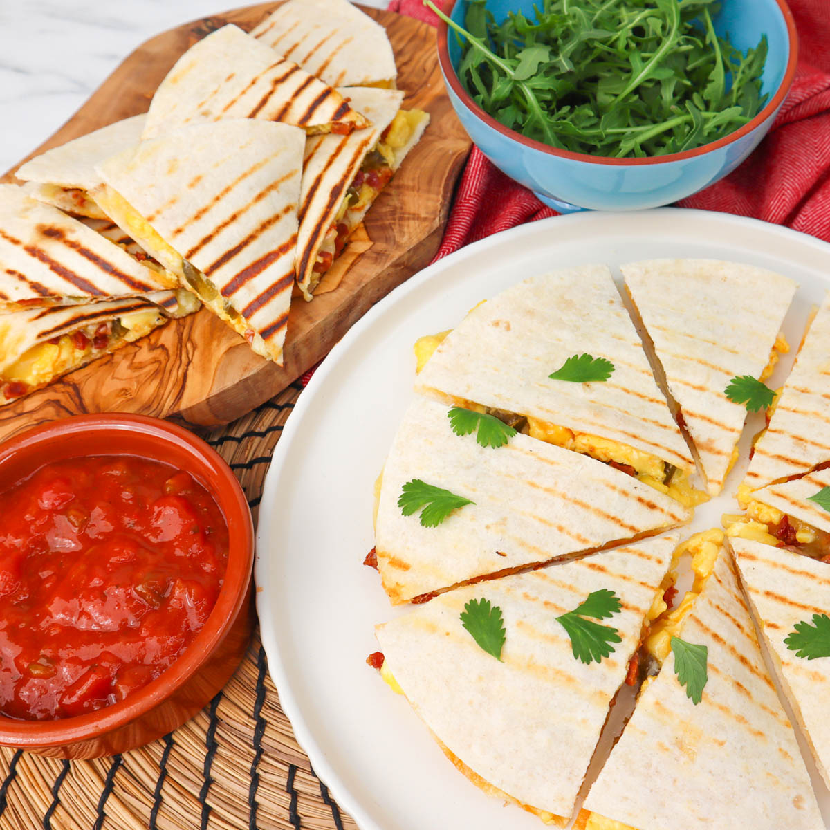 Quesadillas du petit-déjeuner Quesadillas de petit-déjeuner coupées en tranches avec de la coriandre, servies avec de la salsa et une salade de roquette.