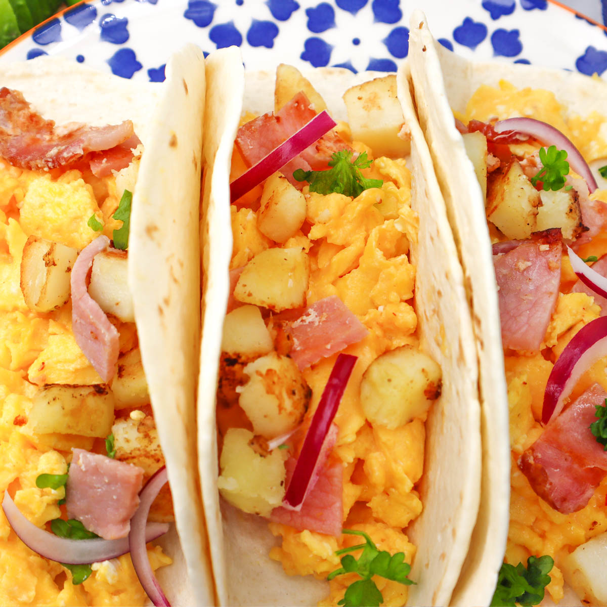 Tacos du petit-déjeuner Trois tacos pour le petit-déjeuner garnis d'œufs brouillés, de pommes de terre, de jambon, et agrémentés d'oignon rouge et de coriandre.