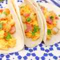 Drei Frühstückstacos gefüllt mit Rührei, Kartoffeln und Schinken, garniert mit Koriander.