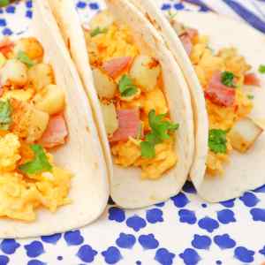 Trois tacos pour le petit-déjeuner garnis d'œufs brouillés, de pommes de terre et de jambon, le tout agrémenté de coriandre.
