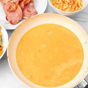 Une poêle avec du beurre fondu crémeux et jaune, pour des tacos au petit-déjeuner, entourée d'autres ingrédients du petit-déjeuner.