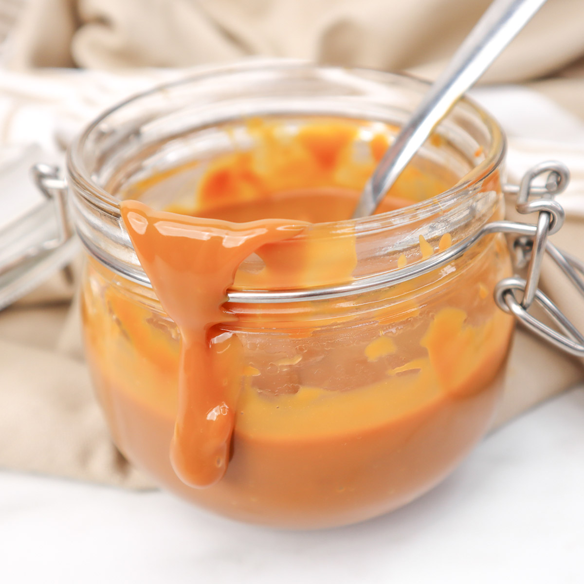 Caramel Sauce A jar of rich caramel sauce with a spoon, dripping down the side.