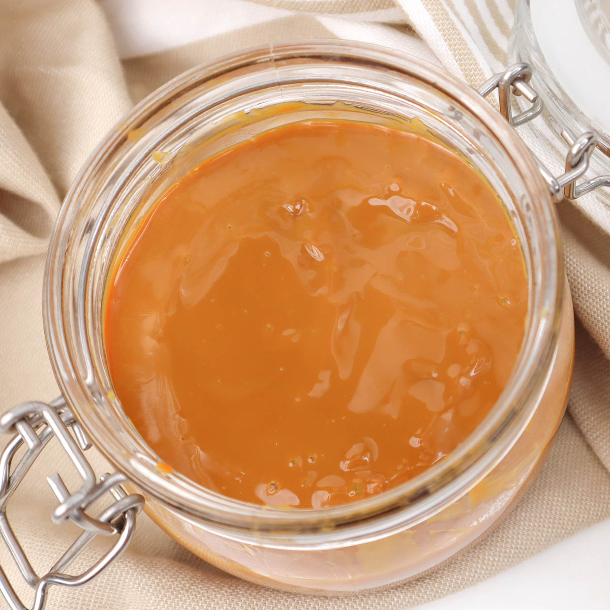 Caramel Sauce A jar filled with smooth caramel sauce, resting on a light fabric background.