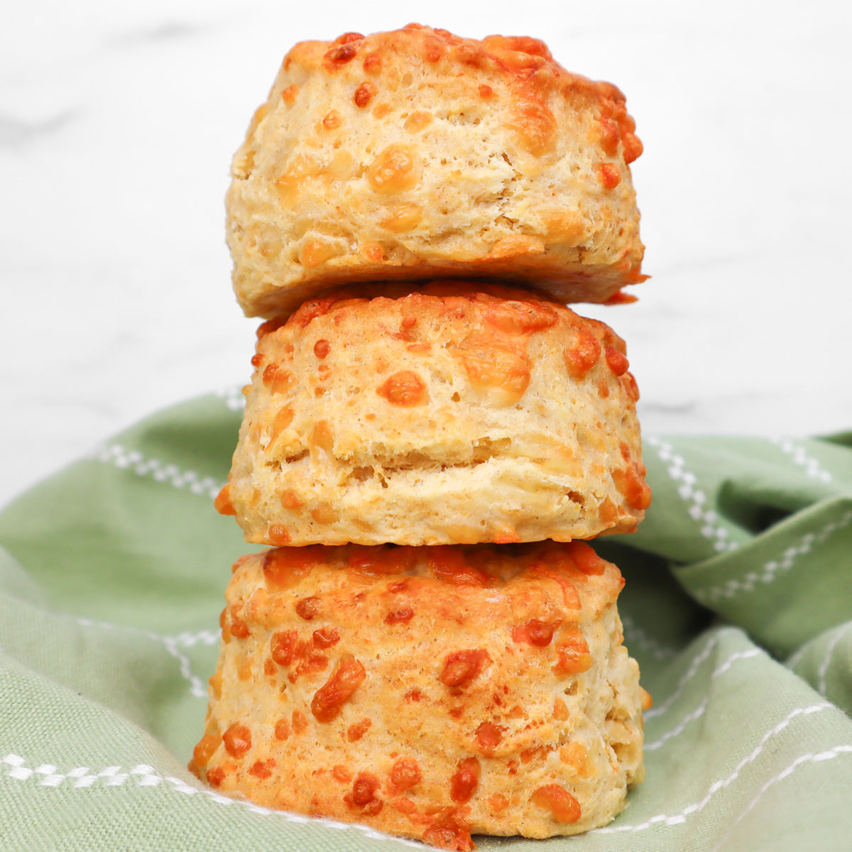 Scones de queijo Três scones de queijo dourados empilhados sobre um pano verde.