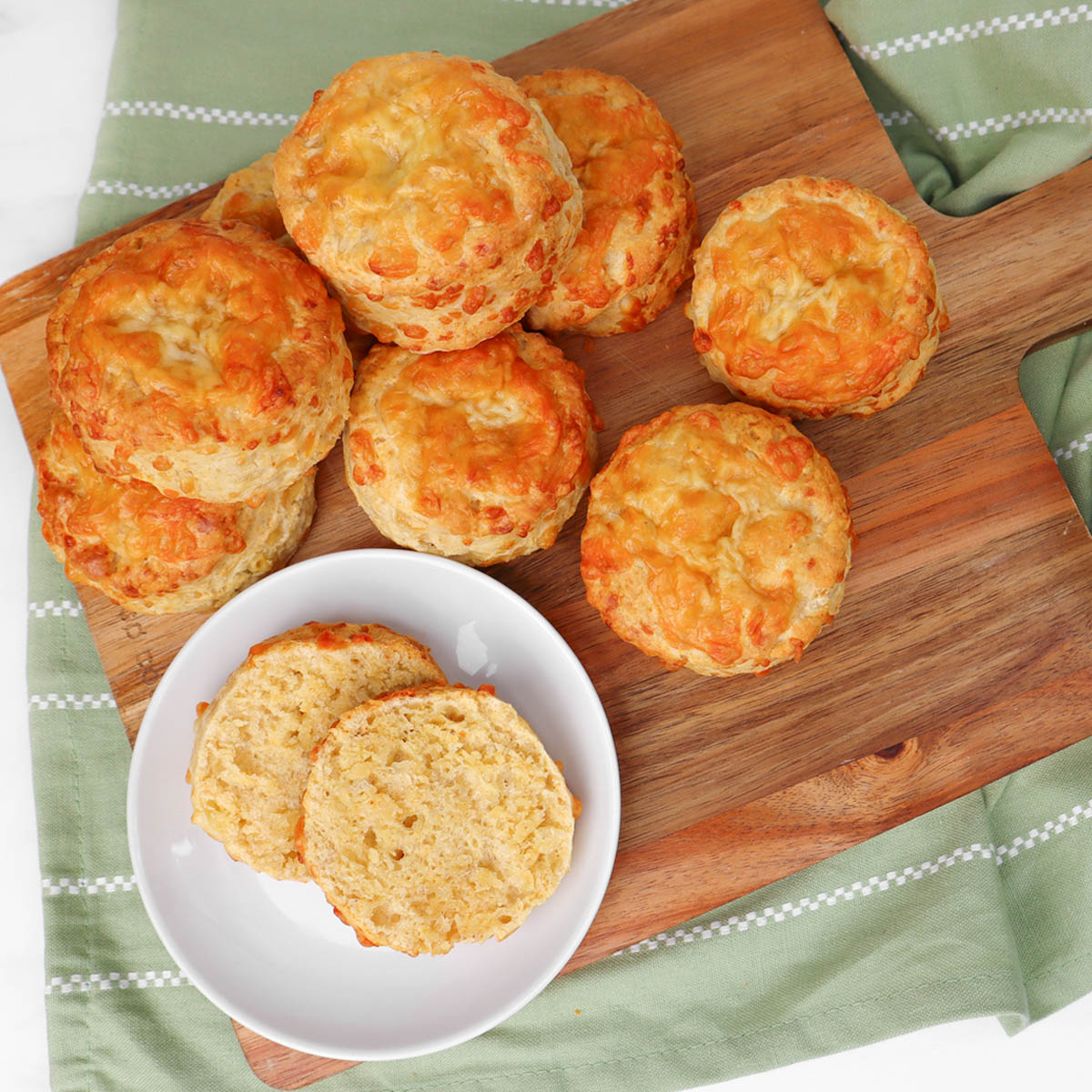 Scones de queijo Scones de queijo frescos, assados na hora, servidos em uma tábua de madeira, acompanhados de um prato com dois scones.