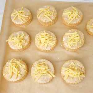 Scones de queijo frescos, assados na hora e cobertos com queijo ralado, servidos sobre papel manteiga.