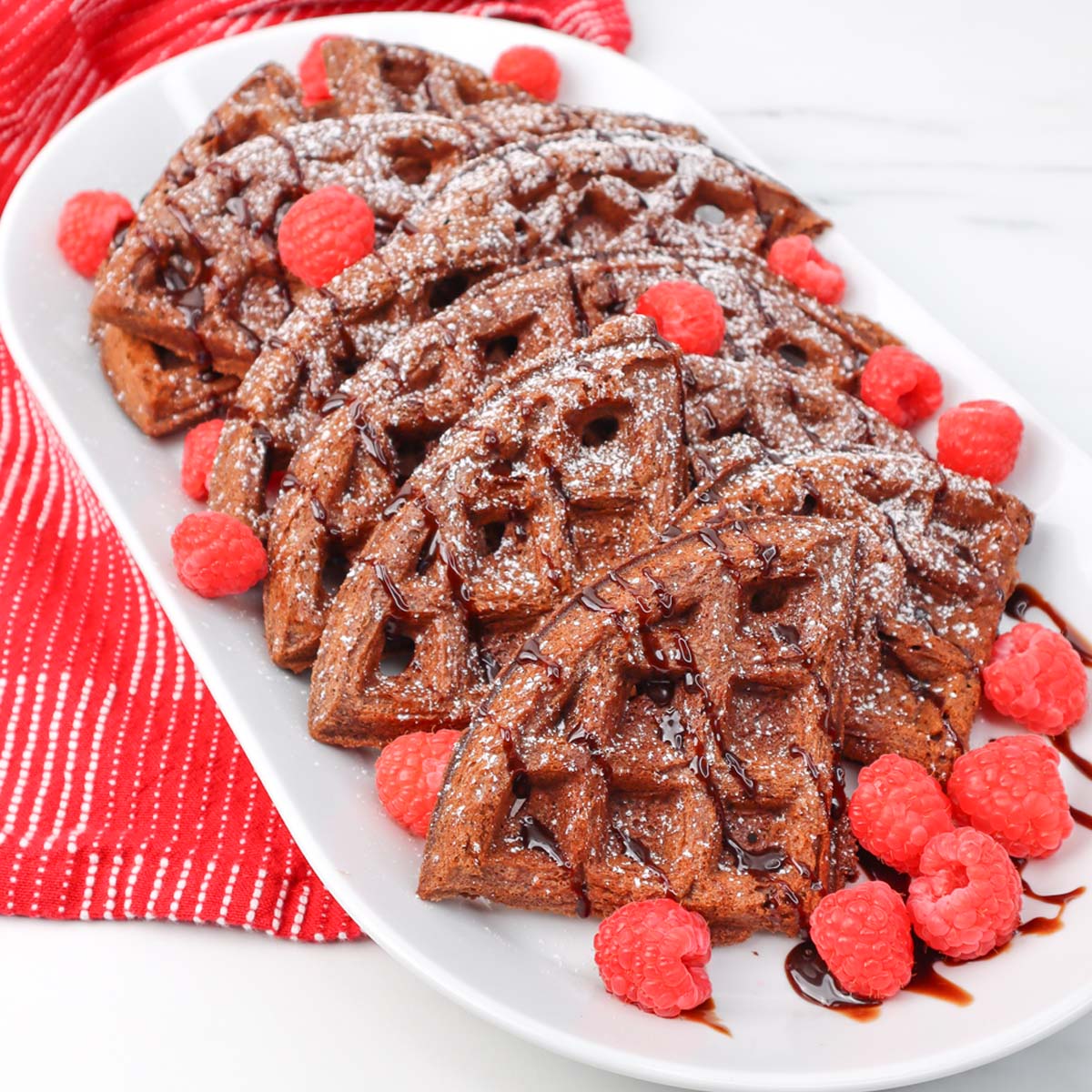 A plate of chocolate waffles topped with raspberries and drizzled with chocolate sauce.