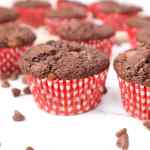 Primer plano de muffins de chocolate y calabacín en moldes de rayas rojas y blancas, con chispas de chocolate esparcidas alrededor.