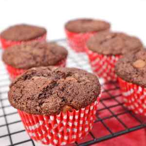 Muffins au chocolat et à la courgette fraîchement sortis du four, dans des caissettes à carreaux rouges, sur une grille de refroidissement.