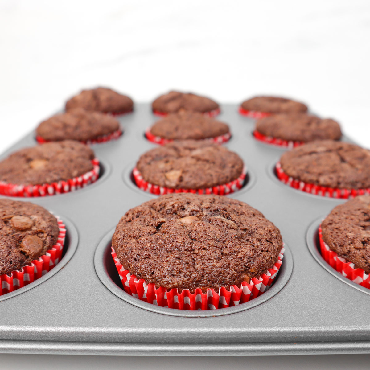 Muffins au chocolat et à la courgette Muffins au chocolat et à la courgette fraîchement cuits dans un moule à muffins avec des caissettes rouges.