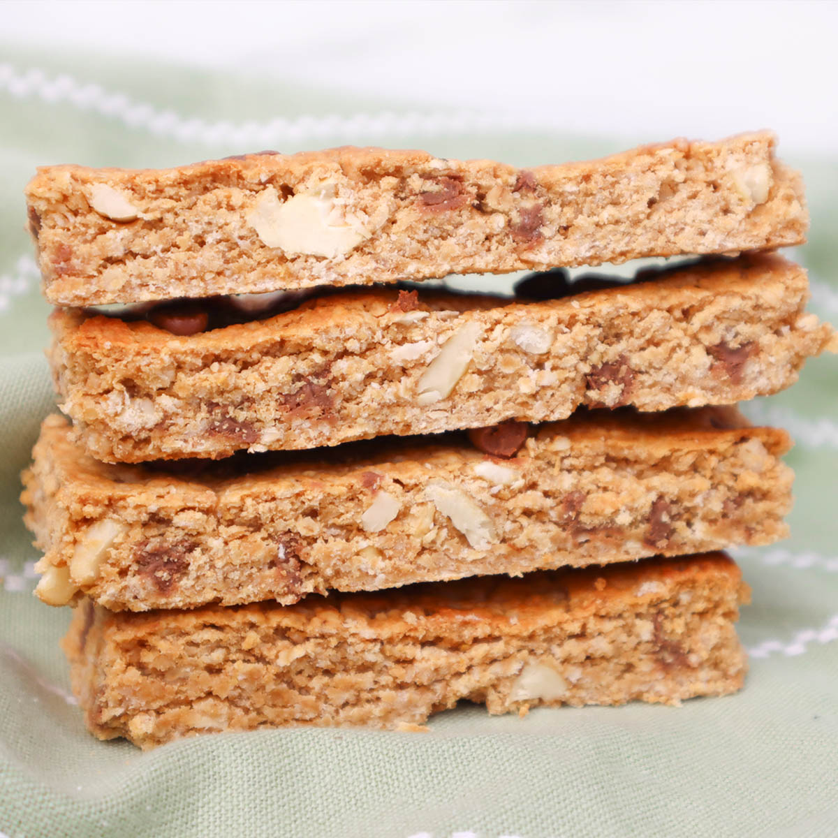 Barres de granola Pile de barres de granola maison aux noix et aux pépites de chocolat sur un tissu vert.