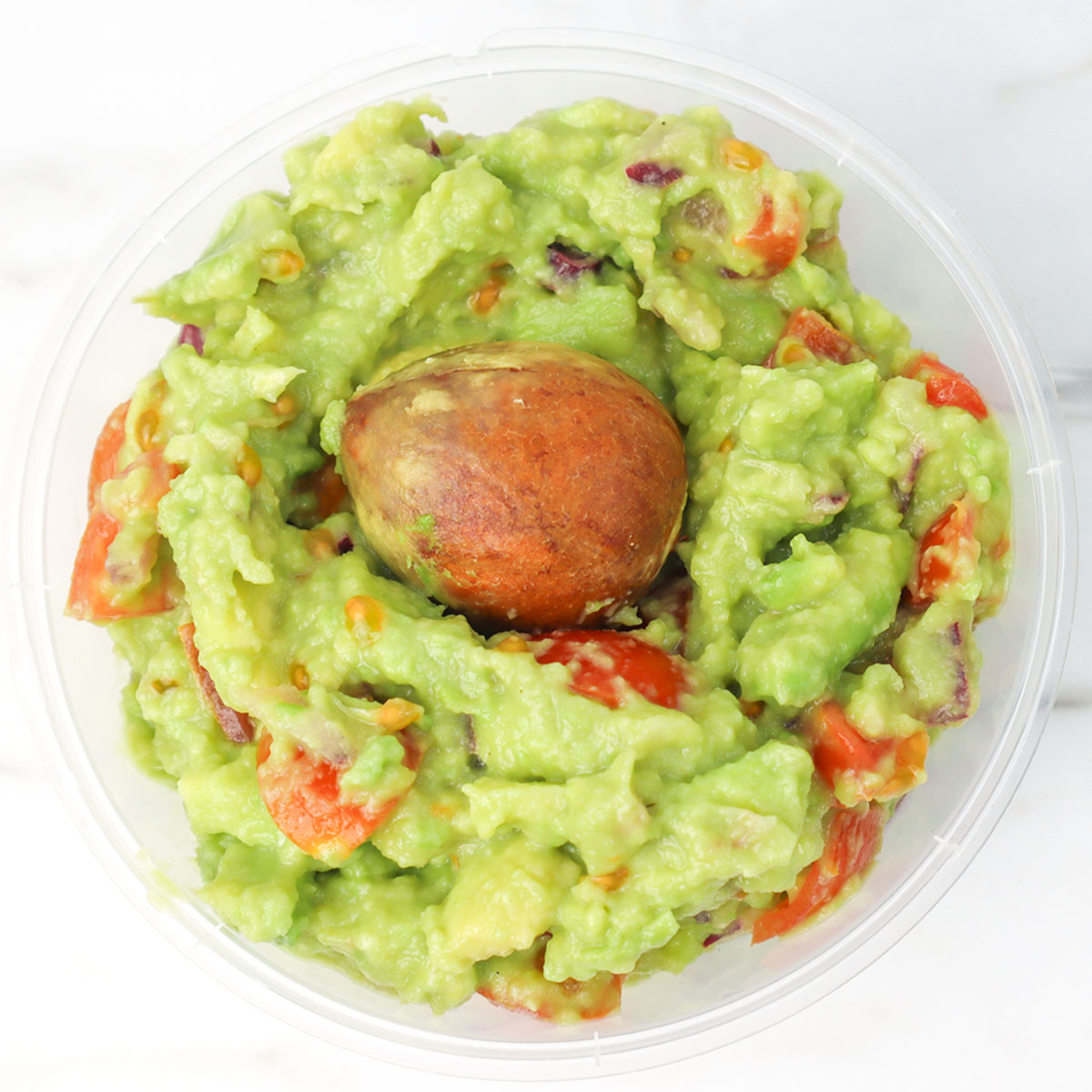 Meilleure recette de guacamole Un bol de guacamole frais avec des tomates en dés et un noyau d'avocat par-dessus.