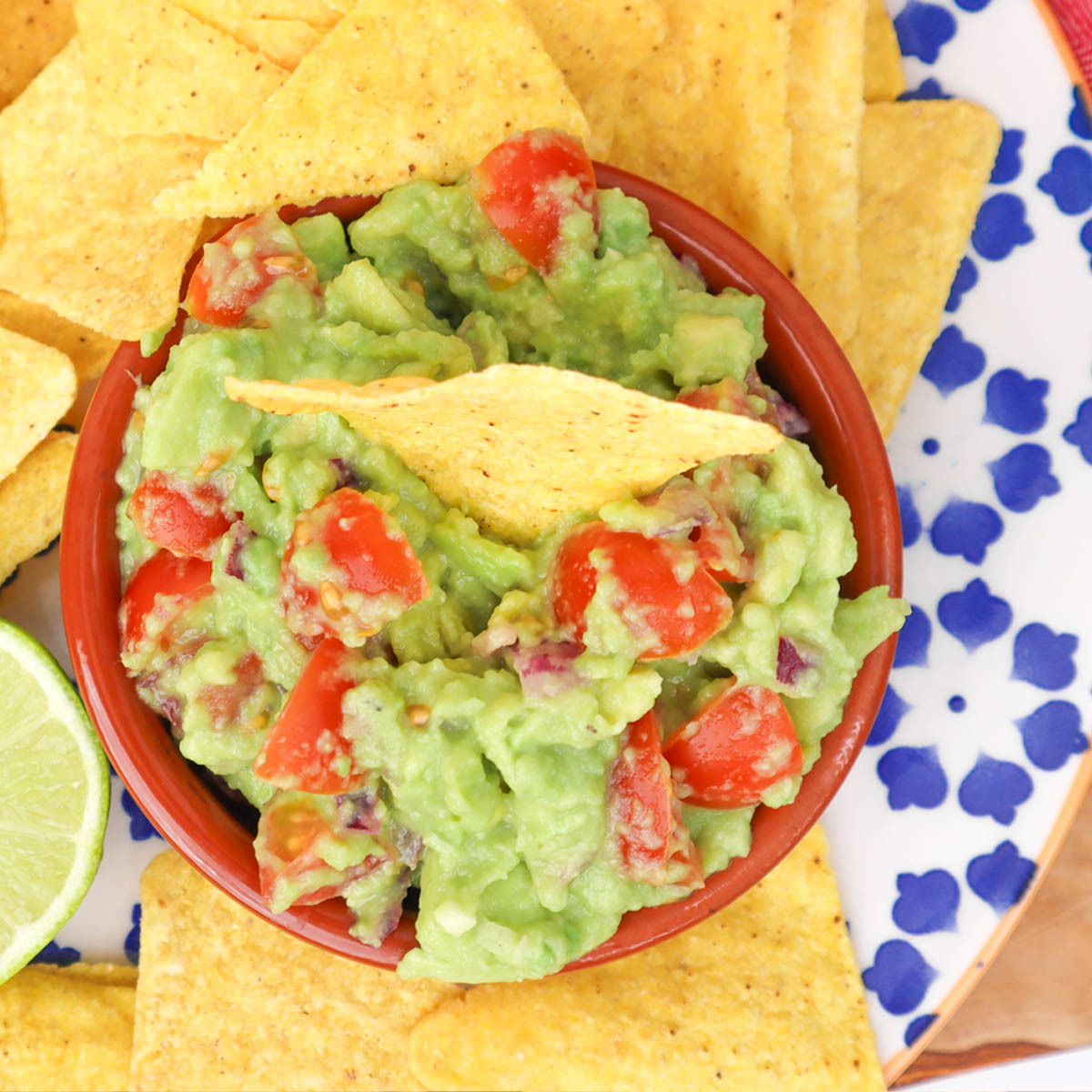 Meilleure recette de guacamole Un bol de guacamole avec des tomates en dés et des chips de tortilla en accompagnement.