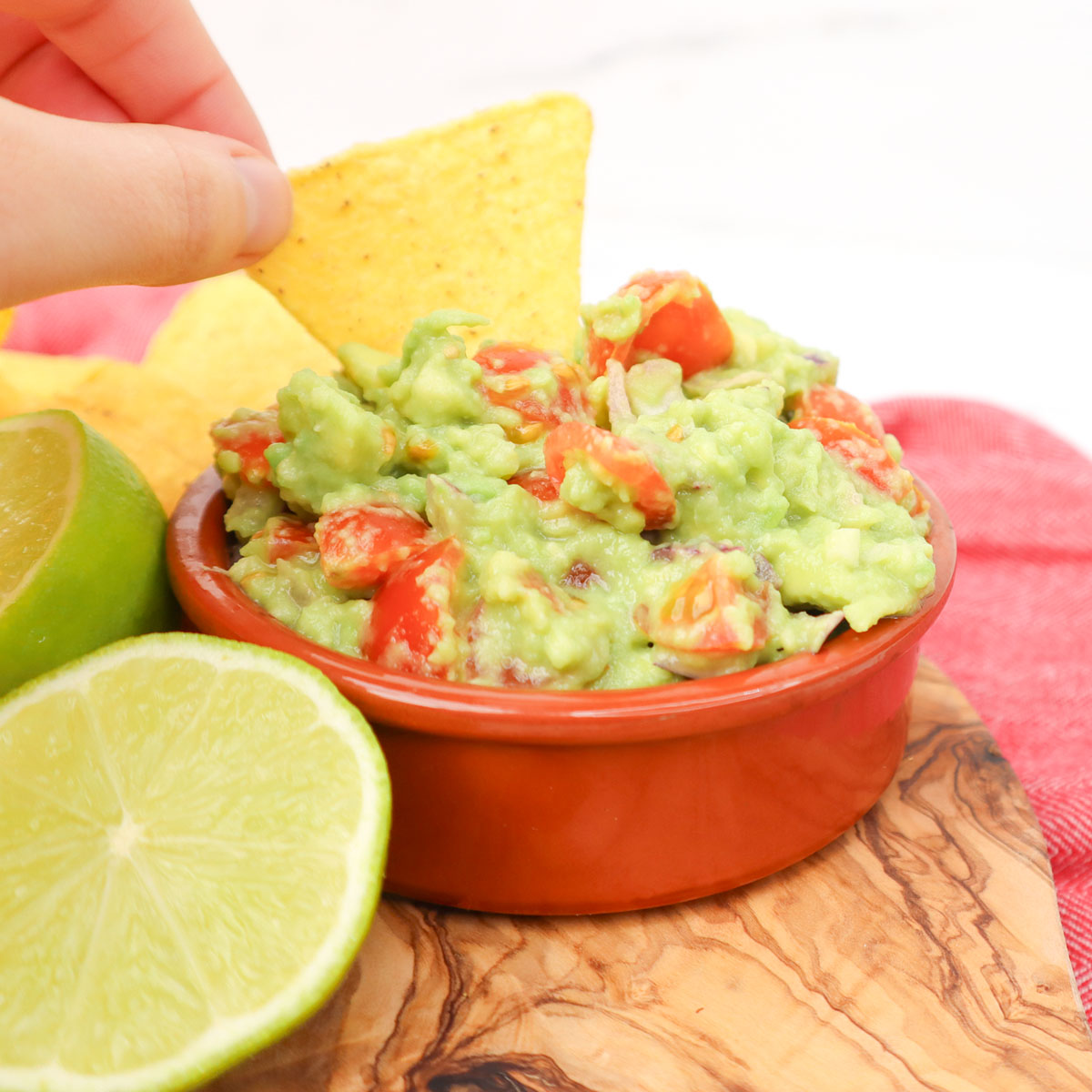 Meilleure recette de guacamole Un bol de guacamole avec des tomates en dés, servi avec une chips de tortilla et des demi-citrons verts.