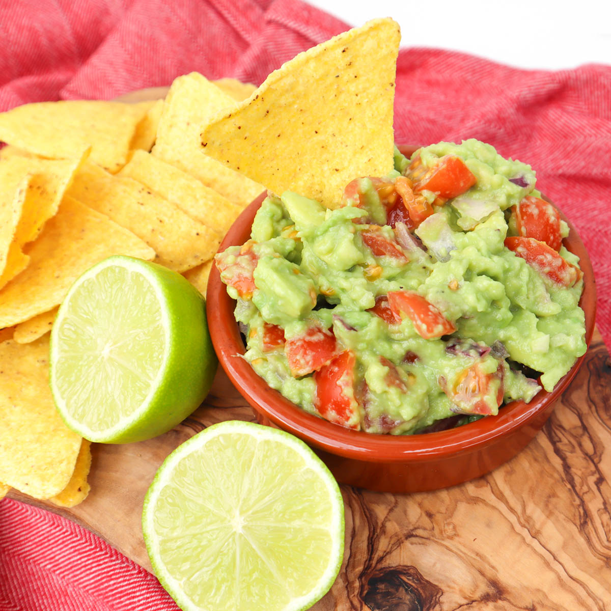 Meilleure recette de guacamole Un bol de guacamole avec des tomates en dés, servi avec des chips de tortilla et des tranches de citron vert.