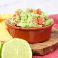 Una ciotola di guacamole con pomodori a cubetti, servita con lime e tortilla chips.