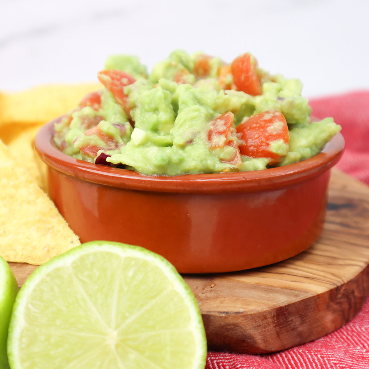 A bowl of guacamole with diced tomatoes, served with lime and tortilla chips.