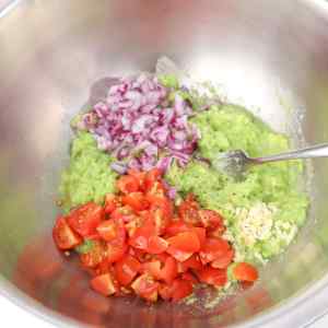 Un bol contenant de la purée d'avocat, des tomates en dés, de l'oignon rouge et de l'ail pour le guacamole.