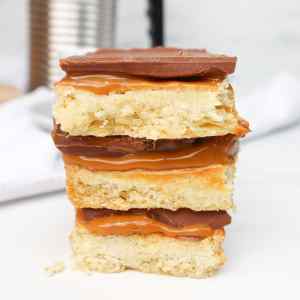 Uma pilha de biscoitos Millionaires Shortbread com camadas de caramelo e chocolate sobre uma base crocante.