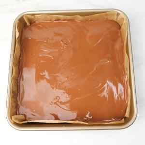 Uma bandeja com chocolate derretido sobre uma base, pronta para endurecer e servir de base para o Millionaires Shortbread.