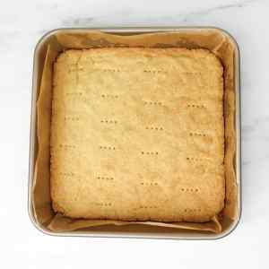 Uma camada quadrada de massa amanteigada em uma assadeira forrada com papel manteiga.