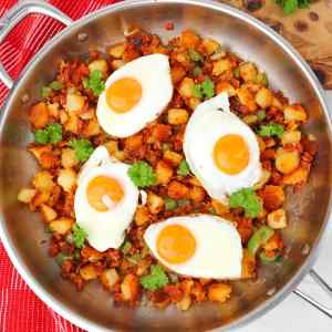 A skillet filled with potato and chorizo hash topped with fried eggs and fresh cilantro.