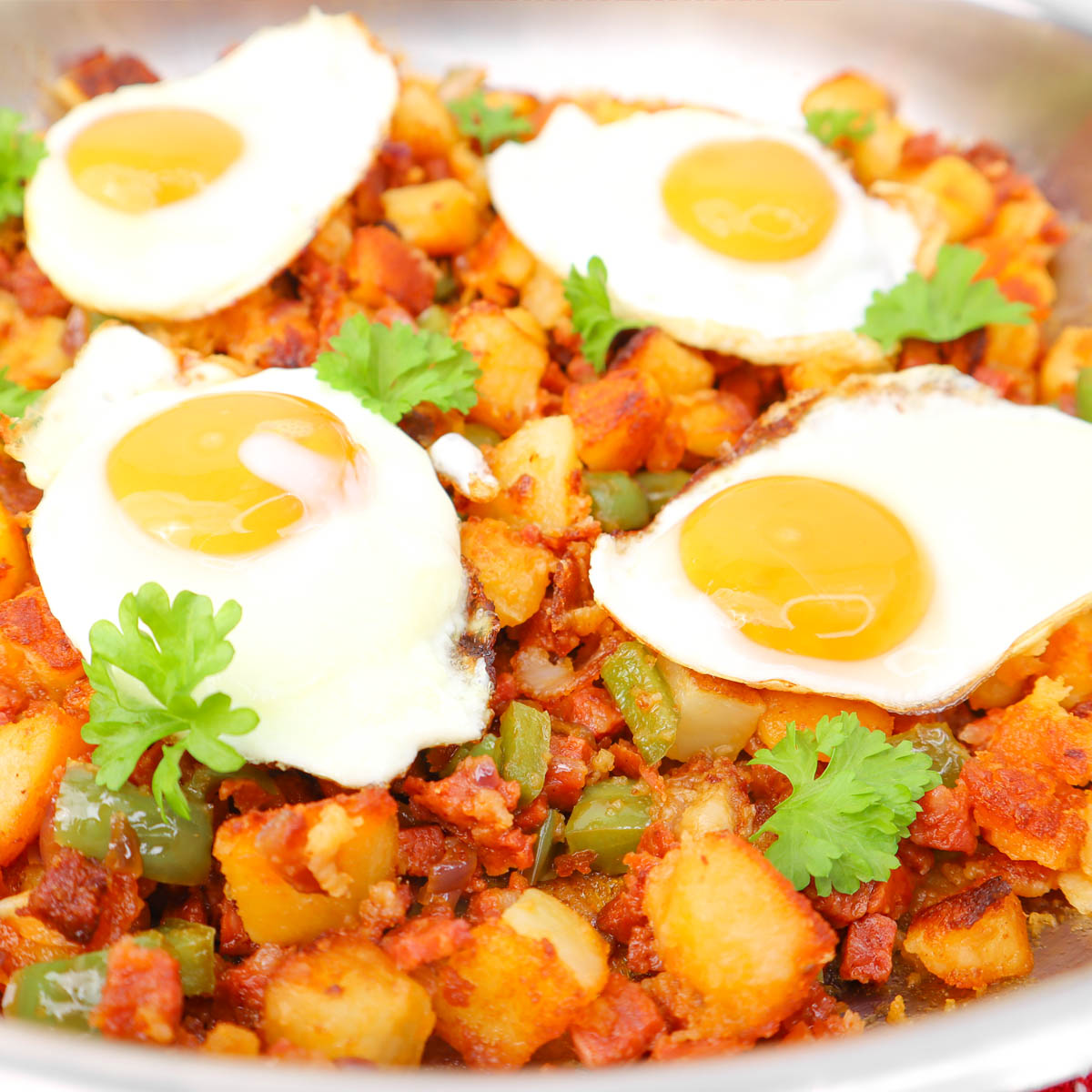 Potato and Chorizo Hash A skillet filled with potato and chorizo hash topped with fried eggs and fresh cilantro.