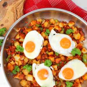 A skillet filled with potato and chorizo hash topped with fried eggs and garnished with cilantro.