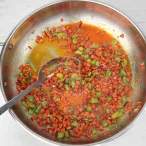 Chopped chorizo and green peppers sautéing in a pan.
