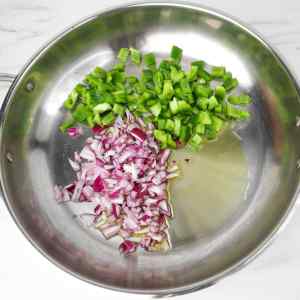 Chopped green bell peppers and red onions in a stainless steel pan.