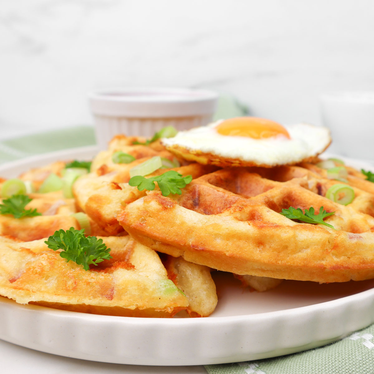 Gaufres salées Une assiette de gaufres salées garnies d'un œuf au plat et parsemées d'oignons verts et de persil.