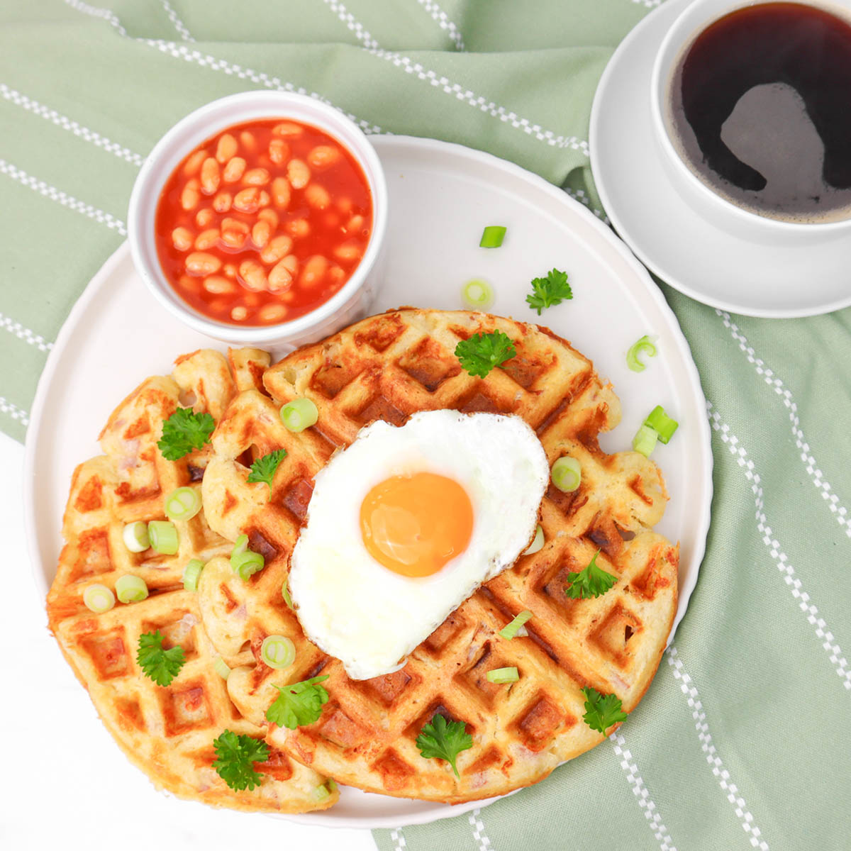 Gaufres salées Gaufres salées garnies d'un œuf au plat, servies avec des haricots blancs à la sauce tomate et parsemées d'oignons verts et de coriandre.