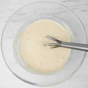 Un bol en verre rempli d'une pâte crémeuse et un fouet posé à l'intérieur.