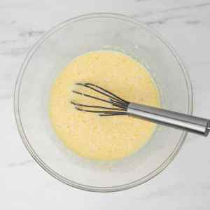 Un bol en verre contenant une pâte jaune avec un fouet à l'intérieur.