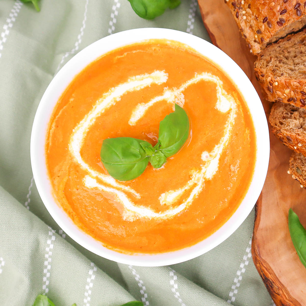 A bowl of creamy tomato soup garnished with basil leaves, served with slices of bread.