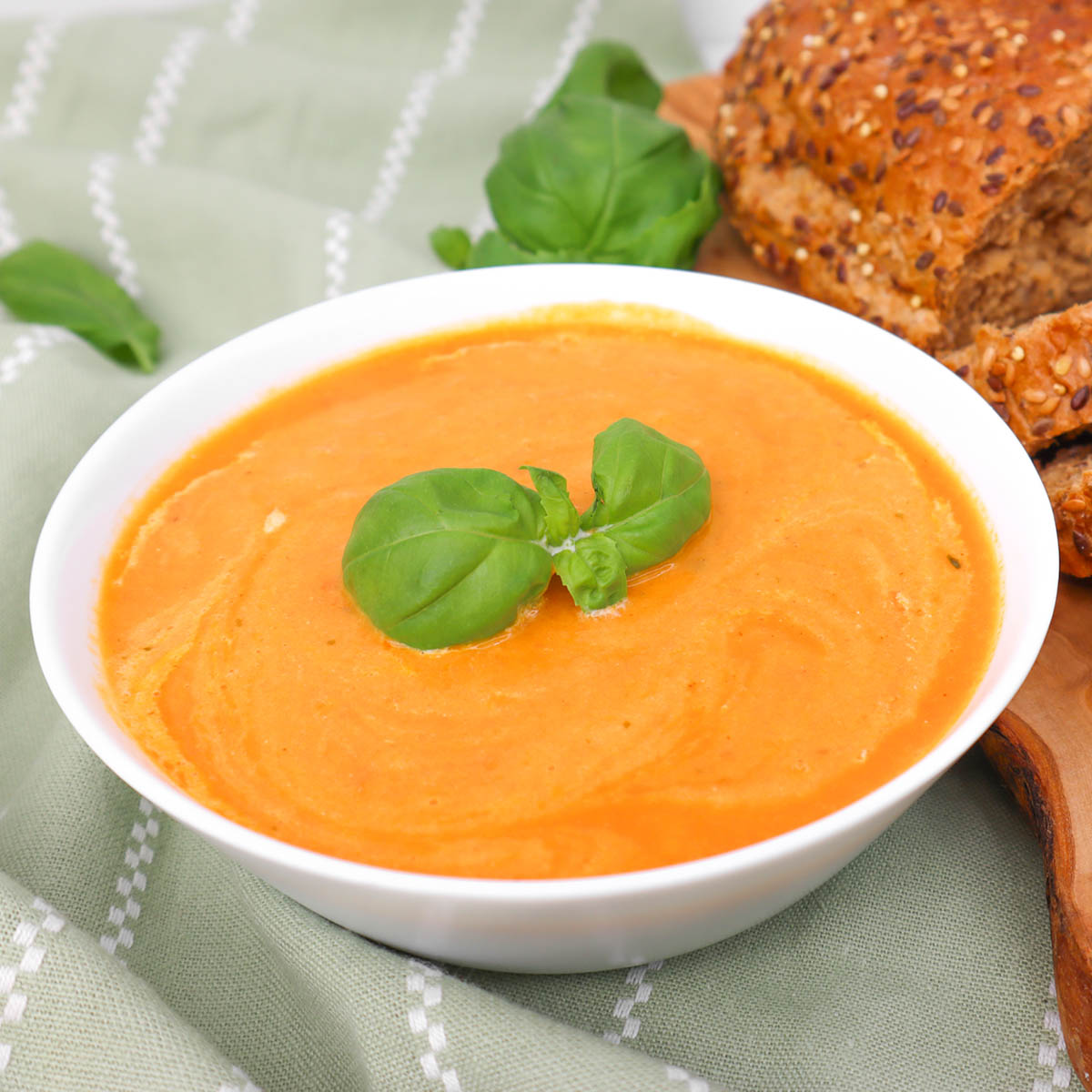 Soupe à la tomate Un bol de soupe crémeuse à la tomate garnie de basilic frais, accompagné d'une tranche de pain au sésame.