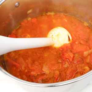 Une casserole de soupe à la tomate est mixée à l'aide d'un mixeur plongeant blanc.