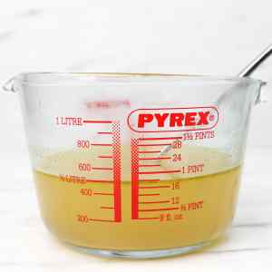 Un verre doseur rempli de bouillon, avec des graduations sur le côté.