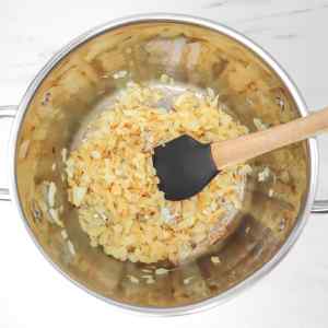 Oignons sautés dans une casserole à l'aide d'une spatule, prêts pour la préparation d'une soupe à la tomate.